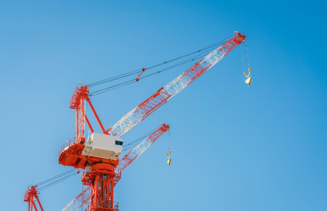 Crane and building construction site Operator using Wolffkran's wireless Intuitive Control remote to maneuver a tower crane lifting steel beams